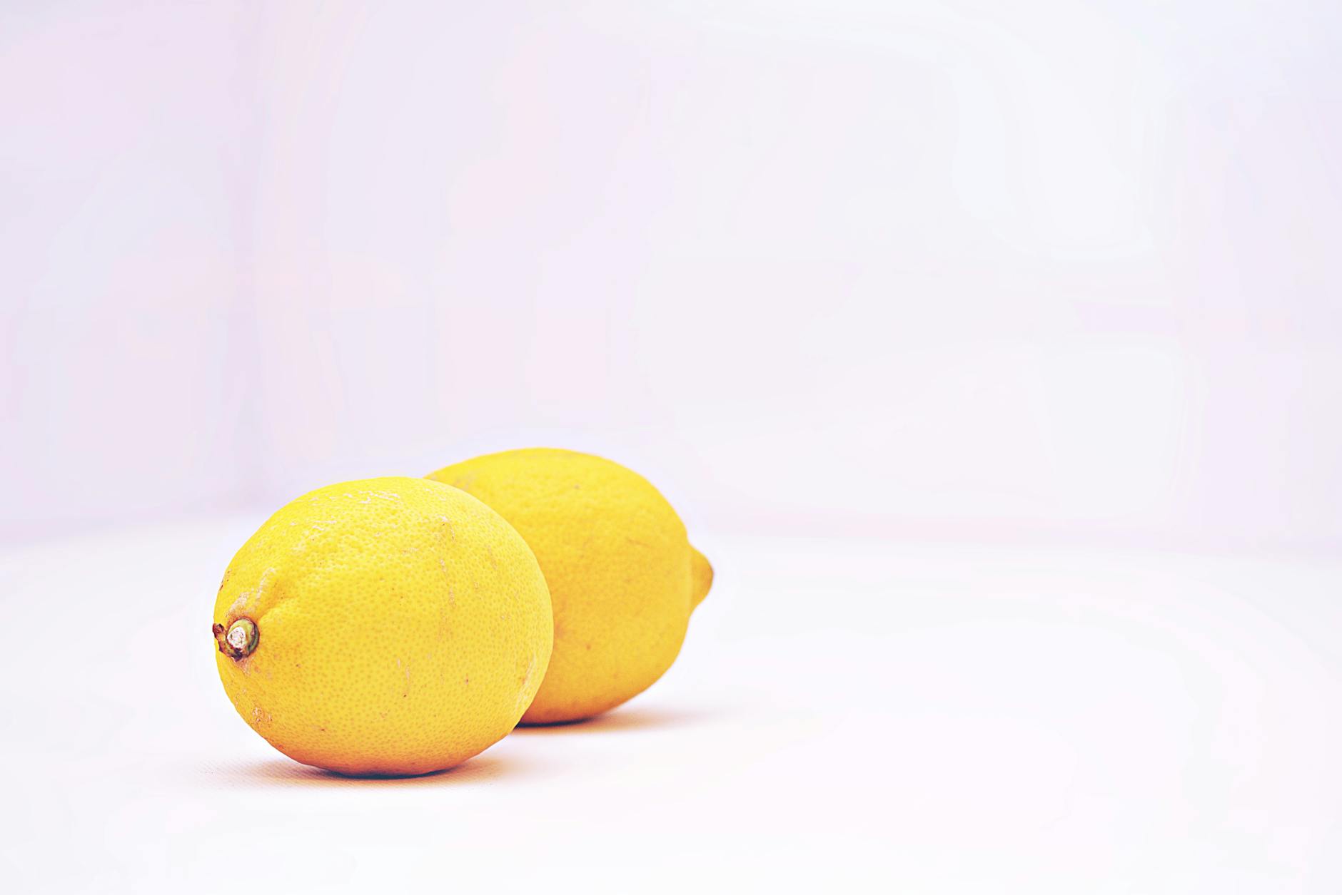 Two vibrant lemons on a minimalistic white background symbolizing fresh, unhurried pleasure