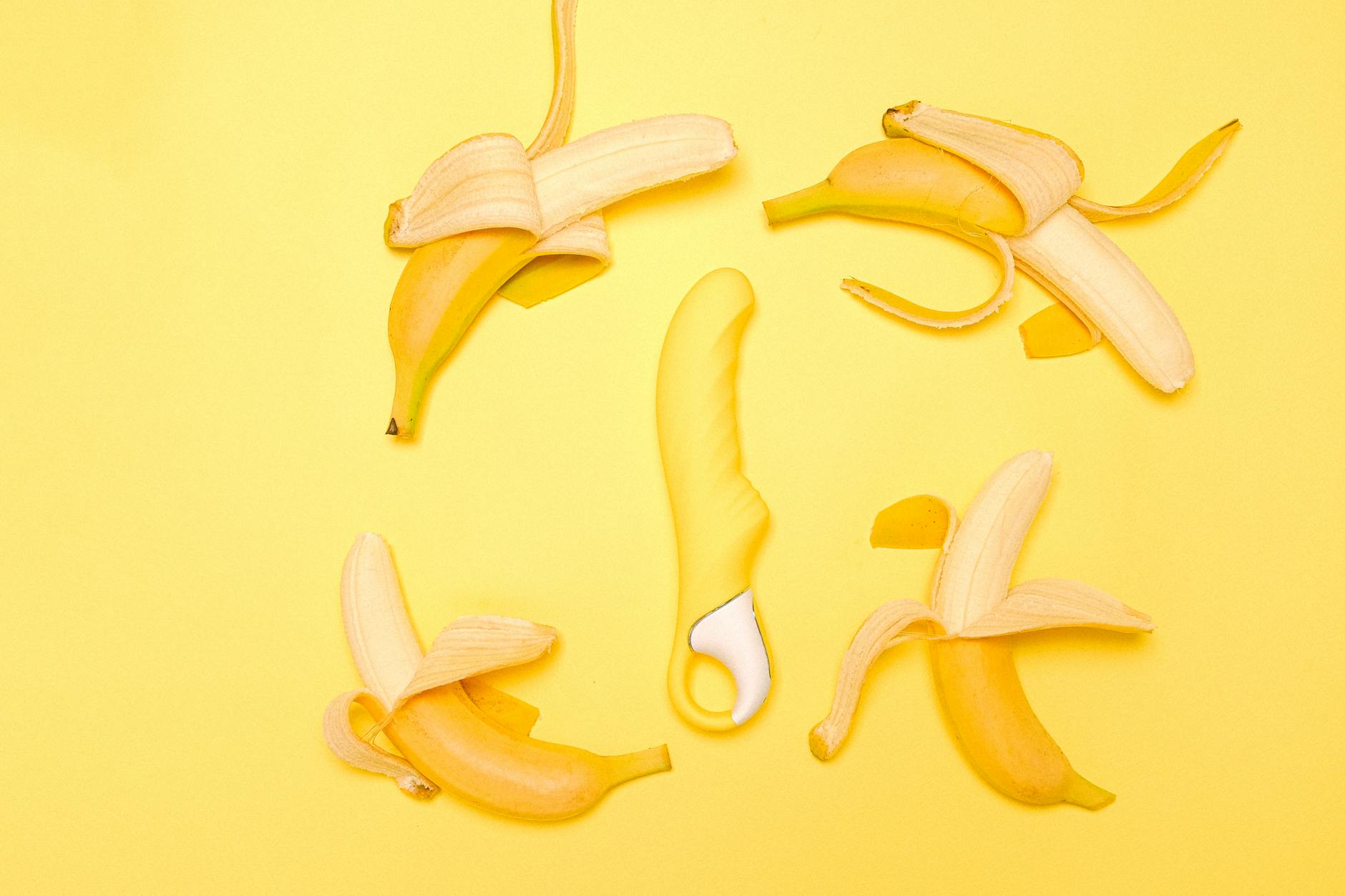Yellow silicone clitoral vibrator surrounded by fresh lemons on bright yellow background